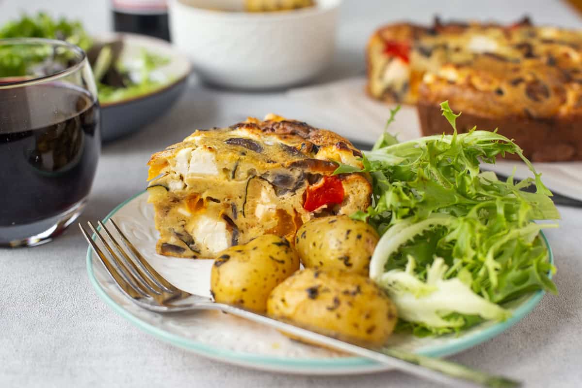A slice of crustless vegetable quiche with potatoes and salad.