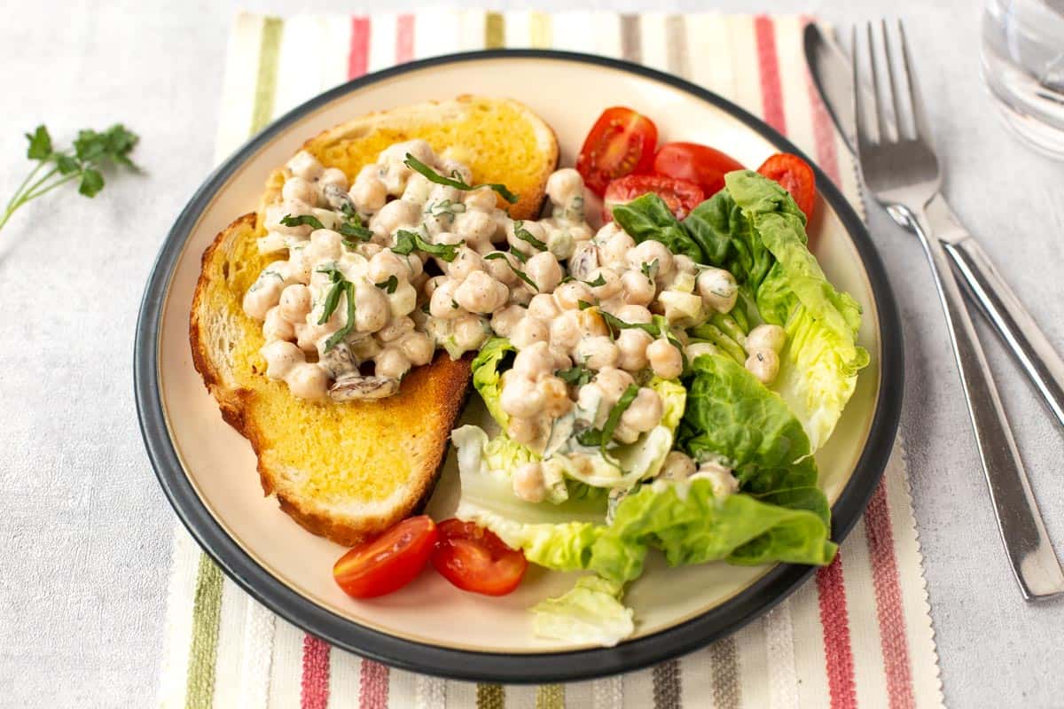 A slice of toast topped with creamy coronation chickpeas, served with salad.