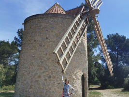 person standing beside a large stone windmill reaching for a rotor blade