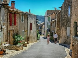 two people walking down a narrow street in Rustrel with old buildings on both sizes