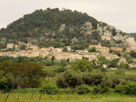 a village of stone buildings on a hillside with the hill rising in the background and agricultural land in the foreground