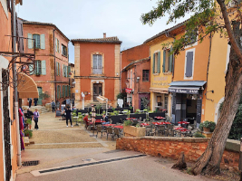 reddish orange and yellow orange buildings in a town square with dining tables along one side
