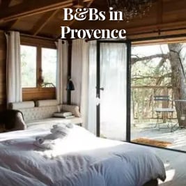 large bed with white linens with view to woods outside an open patio door