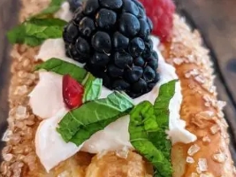 fruit tart with large blackberry on toop of whipped cream and mint leaf