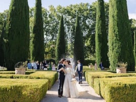 two people getting married in a garden with neatly trimmed hedges and trees