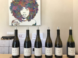bottles of wine lined up on a table with artwork on the wall behind the bottles