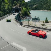 cars on a roadway between forested hills and bright blue water