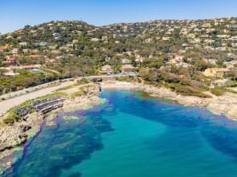 a road beside a shore line with hills covered with trees and houses on the other side of the road