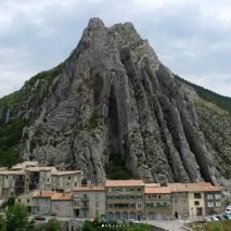 a tall bare stoney mountain with houses in a ring around the base