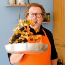 person wearing apron sautéing food in a frying pay