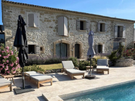 large square stone building shutterss on windows and patio chairs and swimming pool in yard