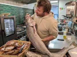 a chef holding a large fish surrounded by seafood in a kitchen