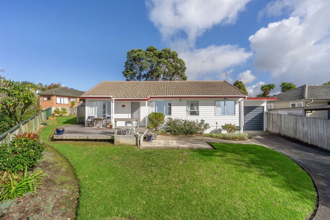 Single-storey white weatherboard house with tiled roof, front deck with outdoor seating and landscaped garden