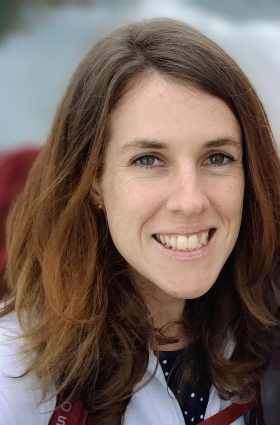 Headshot of Jacki with shoulder-length dark brown hair , smiling at camera from a slight angle with a blurred background.