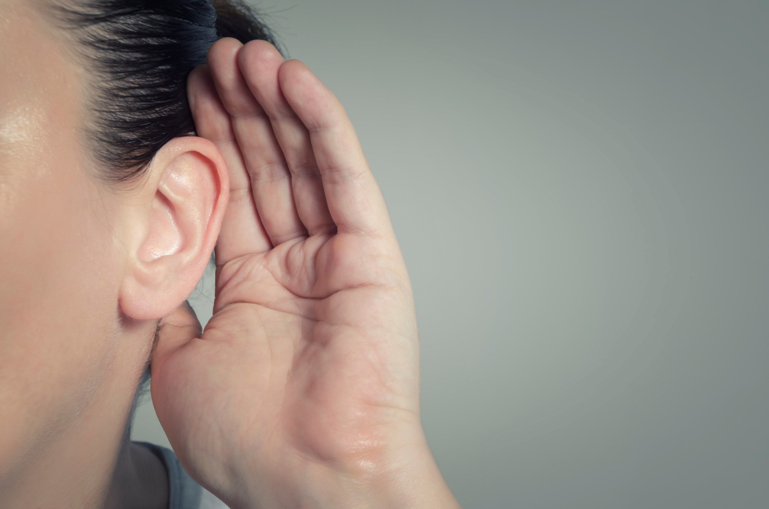 A woman with dark hair holds her hand to her ear.
