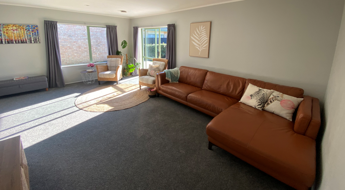 Modern living room with a brown leather sectional, two armchairs by large windows, minimal decor, and soft natural lighting.