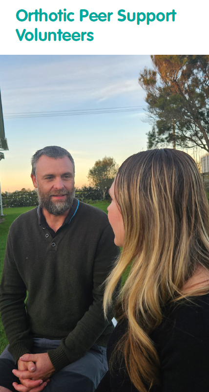 Two people sit on grass outdoors at sunset, talking together. Trees and a building are in the background, and the text “Orthotic Peer Support Volunteers” appears at the top.