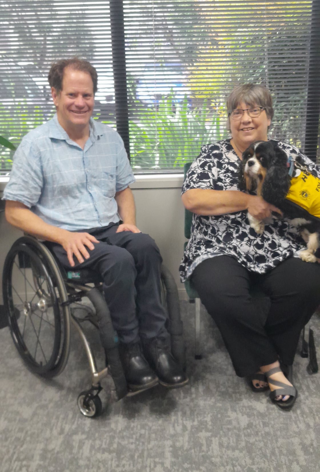 Mike Potter, sitting in a wheelchair on the left, Vanessa Creamer sitting on a chair with her black and white support dog, Balti.