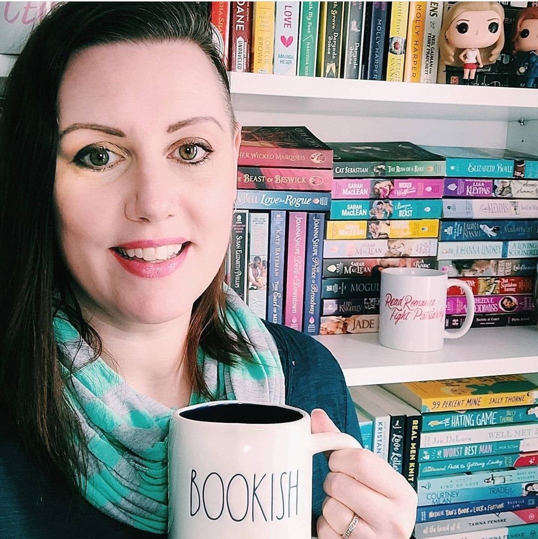 Author Stephanie J. Scott / Stephanie Jayne holding a mug that says Bookish in front of romance books on a bookshelf