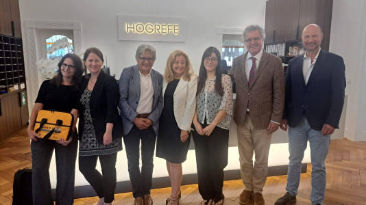 fotografía en donde aparecen 7 personas de pie, sonriendo y mirando hacía adelante. Al fondo hay una cartel que dice Hogrefe y las personas de izquierda a derecha son: Julia Vogt, Nadine Schuchart, Ricardo Rosas, Annemarie Fritz, Victoria espinoza, Jürgen Hogrefe y Jörg Hampe.