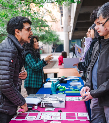 Imagen en la que aparecen desde lado algunas personas presentando en unos stand, mientras otras personas los visitas.