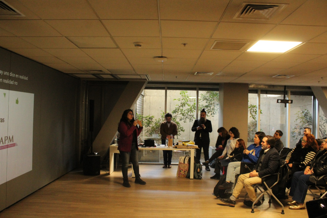 Imagen en donde se aprecia a Polín Olguín presentando una proyección y personas que la están mirando desde una audiencia.