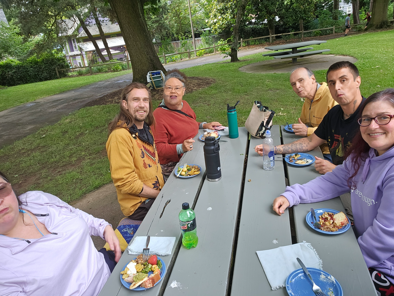 Sitting at the picnic table, you see 3 Sorores and 3 Fratres enjoying a snack together while smiling for the camera.