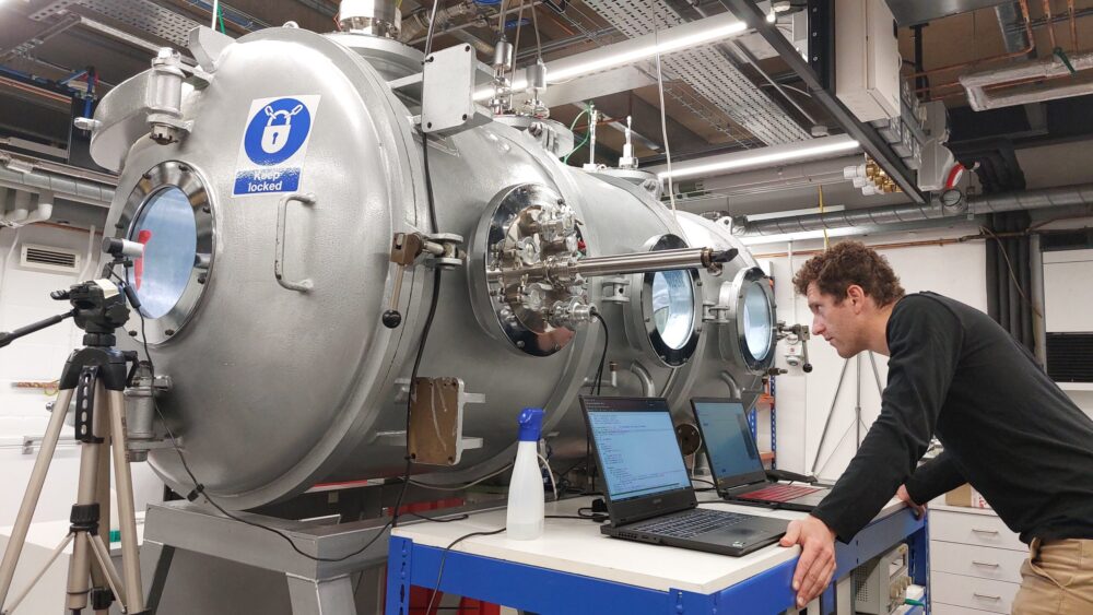 Male scientist looking at laptops in front of low pressure chamber