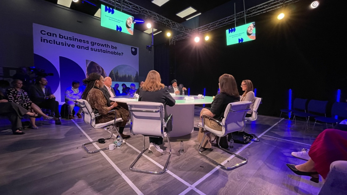 Business professionals sat on a table with an audience watching them