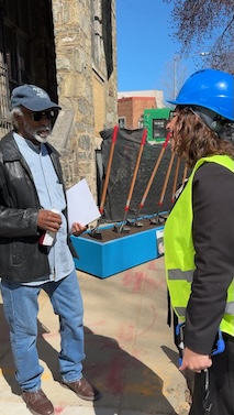 Man in baseball hat with clipboard talks with Councilmember Nadeau in high viz vest and hard hat