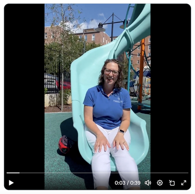Councilmember Nadeau sits on a slide at a playground at Oyster Adams School