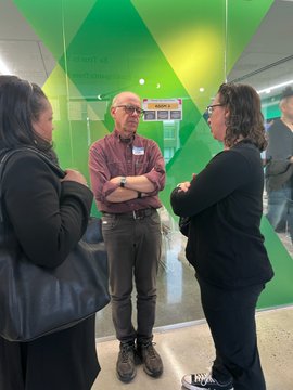 Councilmember Brianne Nadeau in conversation with one woman and one man in front of green glass wall
