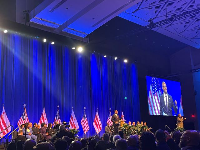 Wide shot of the stage at Washington Convention Center for swearing in ceremony. CM Felder is speaking and appears on jumbotron.