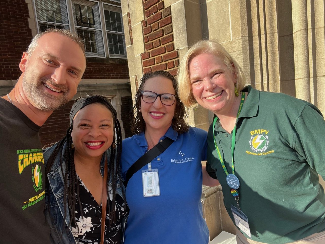 Four people, including Councilmember Nadeau, pose for a photo in front of a school building