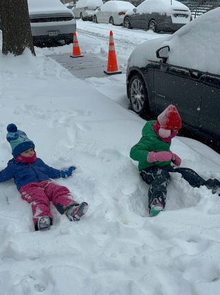 Two girls make snow angels on the sidewalk