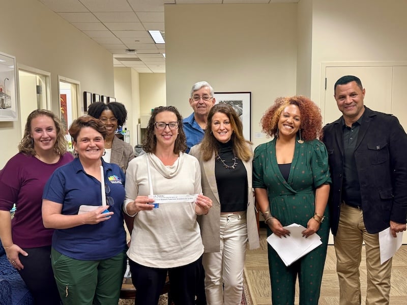 Councilmember Nadeau poses with several people in her office while holding up a slip of paper that says support nonprofits