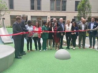 A group of people hold a red ribbon in front of an apartment building at a ribbon cutting ceremony