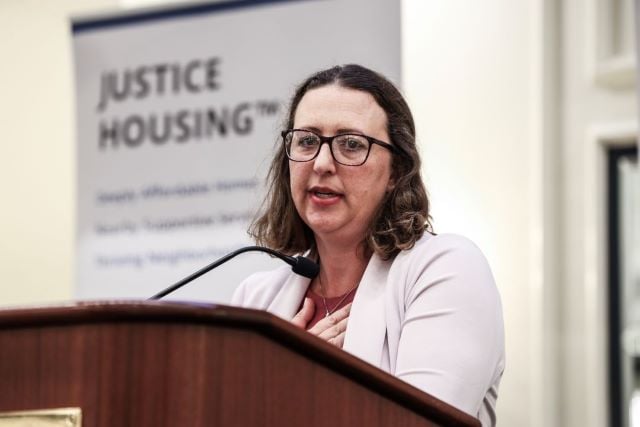 Councilmember Nadeau speaks at a podium with a sign for Justice Housing in the background