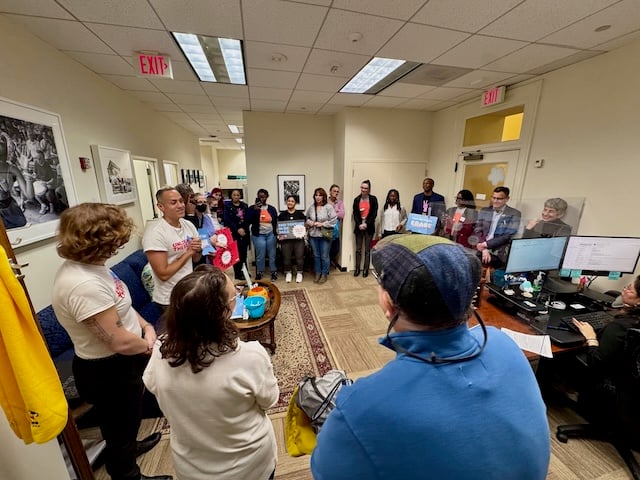 Councilmember Nadeau, foreground back turned to camera, listens as members of the ERASE coalition speak. Some are holding signs saying end solitary confinement