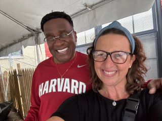 Councilmember Nadeau and a man wearing a red Harvard sweatshirt pose for a selfie under a tent.