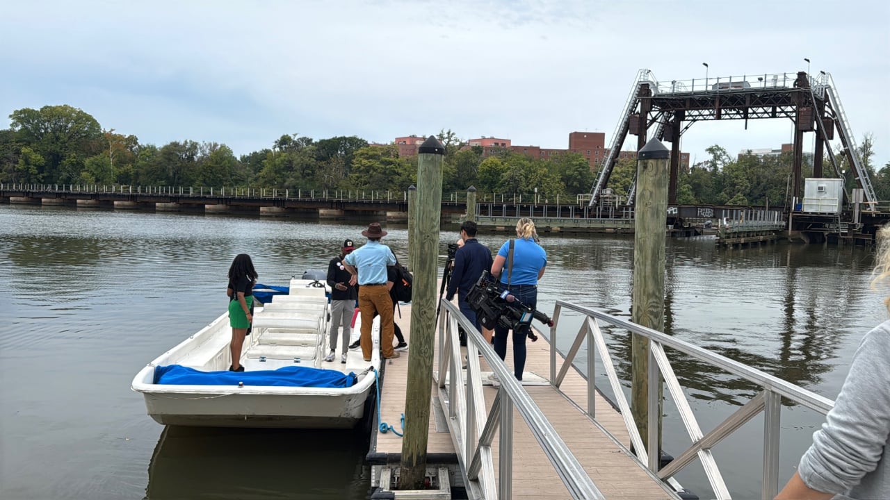 Photo of boat at dock in Anacostia River with people starting to board as others make their way down the ramp