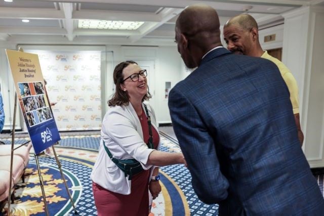 Brianne Nadeau shakes hands with a man in a blue suit whose back is to the camera while another man looks on.