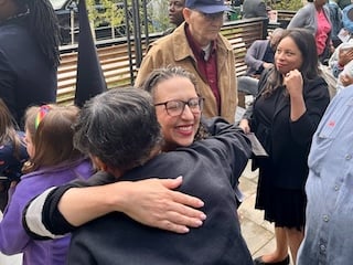 Councilmember Nadeau hugs another person whose back is to the camera and smiles. Others are standing nearby.