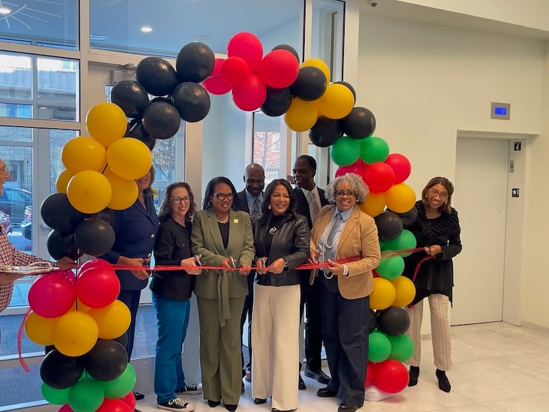 Councilmember Brianne Nadeau joins seven other individuals standing behind a red ribbon and under a balloon arch at a ceremonial ribbon cutting at a new apartment building