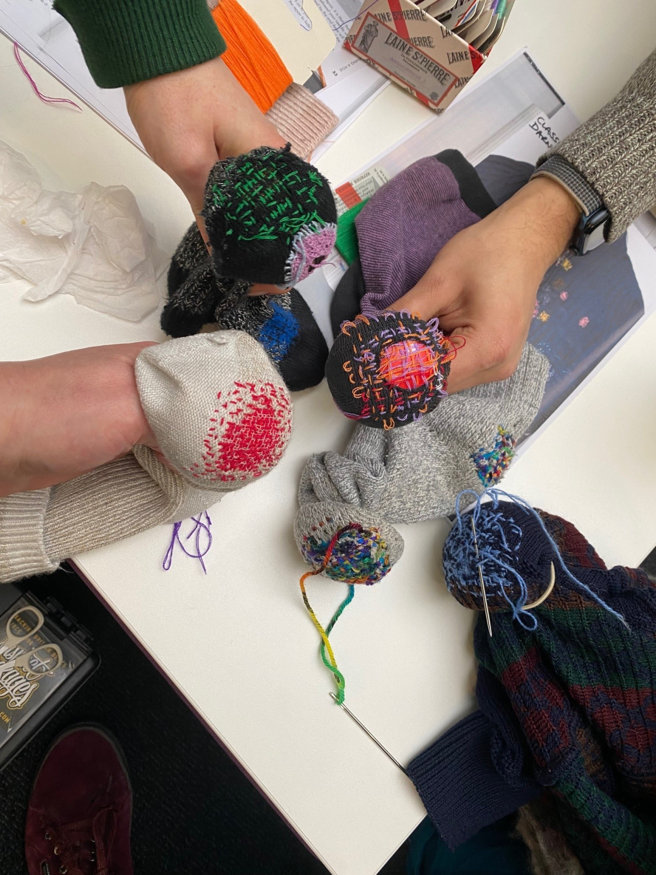 Several hands hold darning mushrooms with socks on them