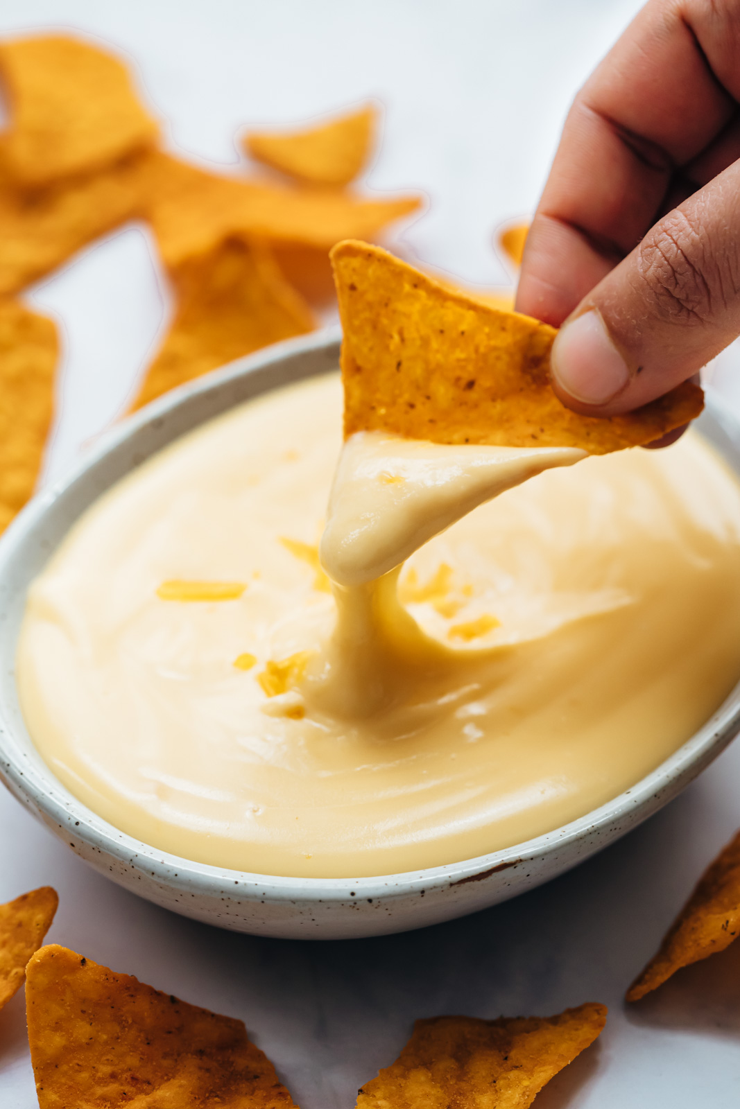 A piece of nacho being dipped into cheese sauce
