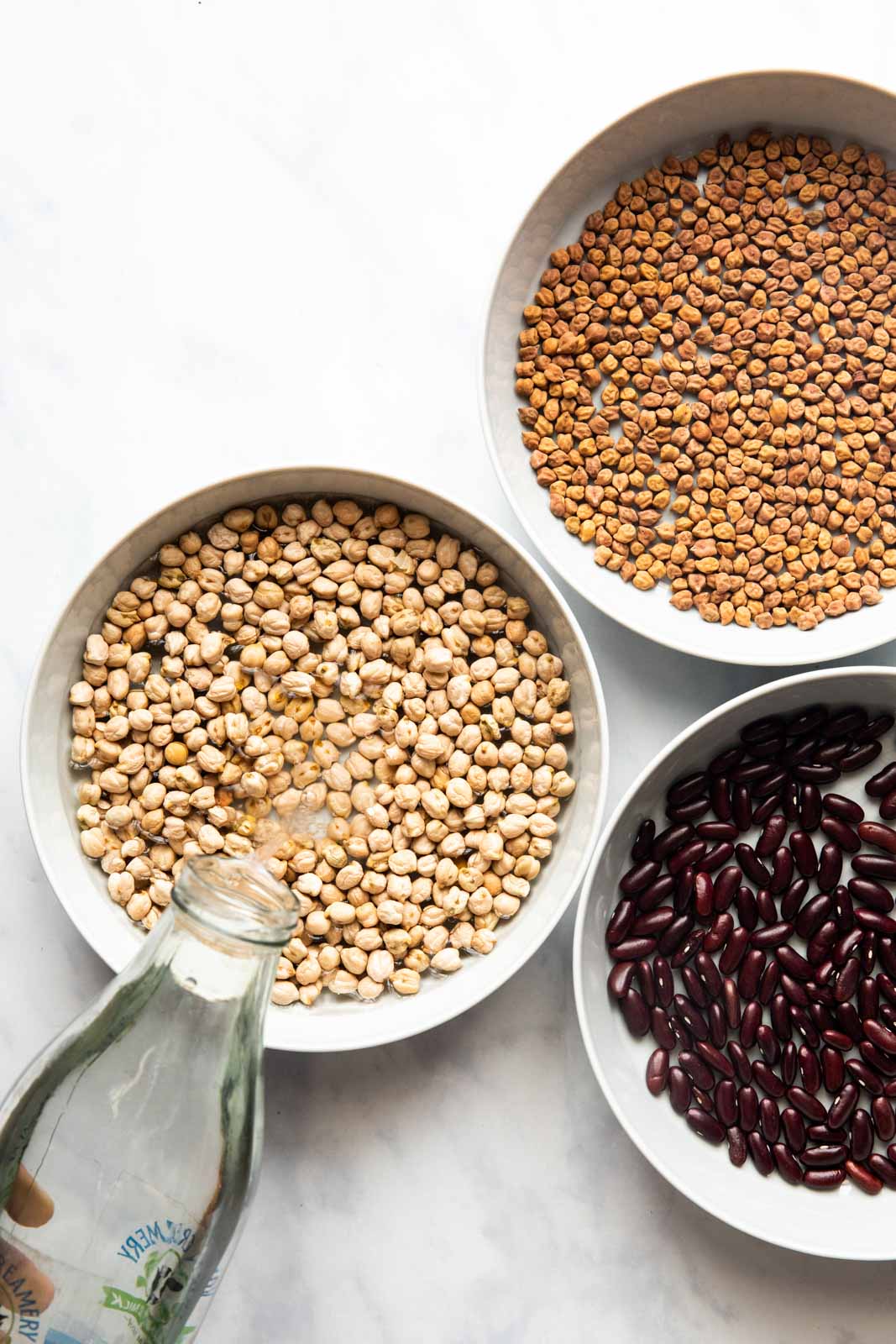 Three bowls filled with beans and a bottle of water being poured into one of the bowls