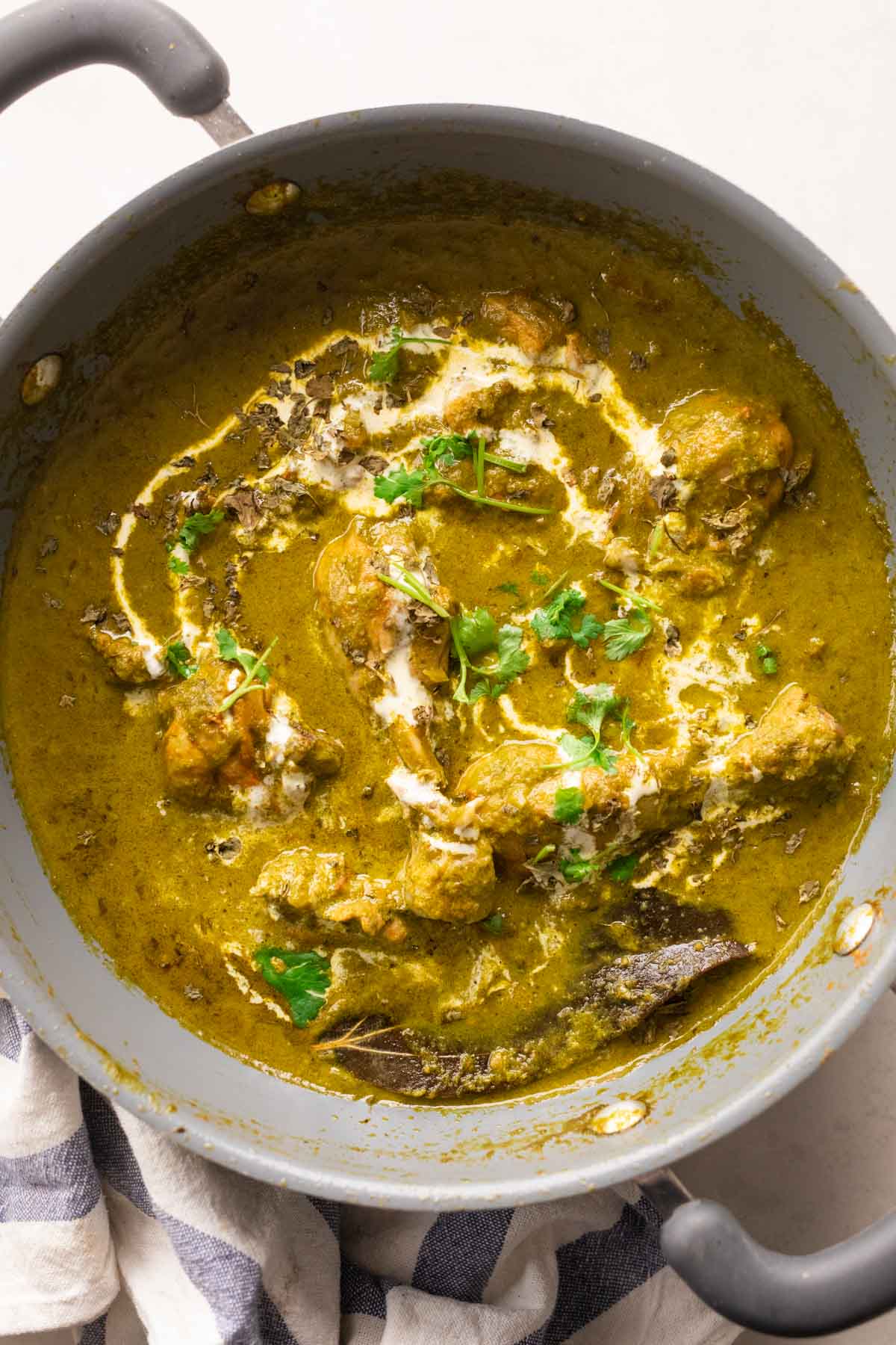 Chicken in a green palak gravy in a grey kadai topped with a drizzle of cream